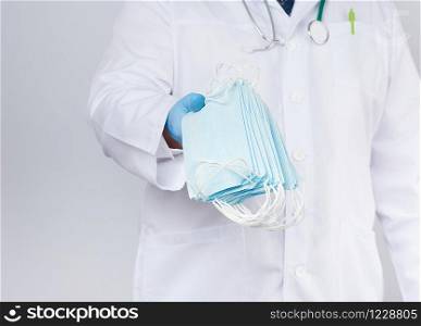 doctor in a white coat, blue latex sterile gloves holds textile medical masks in his hand, protective accessory against viruses and bacteria, close up