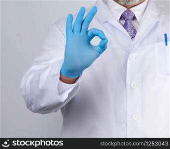 doctor in a white coat with buttons shows a gesture ok with his hands, wearing blue medical gloves, emotion of agreement and approval