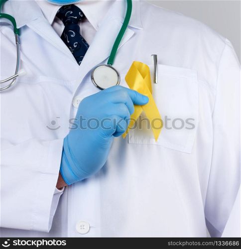 doctor in a white uniform and sterile latex gloves holds a yellow ribbon in his hand, symbol of the fight against the cat&rsquo;s tumor, problem of suicides and their prevention, close up