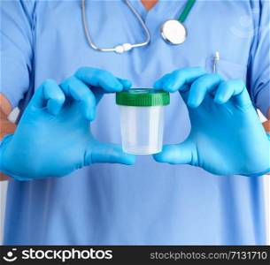 doctor in blue uniform and latex gloves is holding an empty plastic container for taking urine samples, concept of timely diagnosis