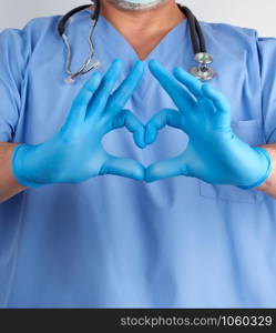 doctor in blue uniform and latex gloves shows a heart gesture near his chest, white background