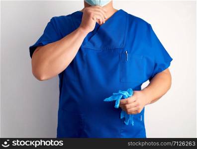 doctor in blue uniform holds sterile latex gloves and puts on a mask, white background