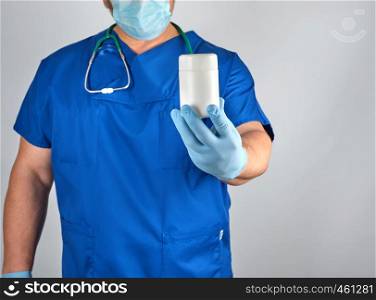 doctor in blue uniform is holding a plastic white jar with pills, gray background