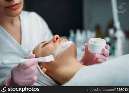 Doctor in gloves rubs the cream on female patient face, cosmetology clinic. Facial skincare, rejuvenation procedure in spa salon. Doctor in gloves rubs the cream on patient face