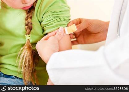Doctor in her practice putting a bandage on some hurt of a little girl child (focus on thumb of doctor)