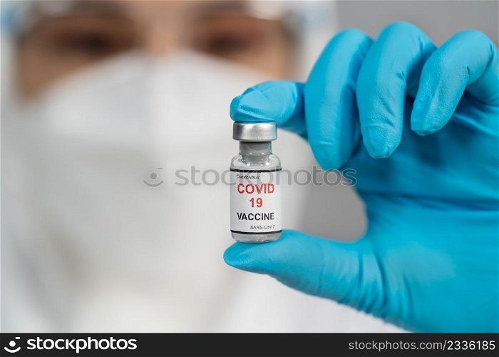 doctor in protective PPE suit holding and gently shaking Coronavirus  Covid-19  vaccine bottle
