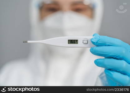 doctor in protective PPE suit holding digital thermometer with normal temperature