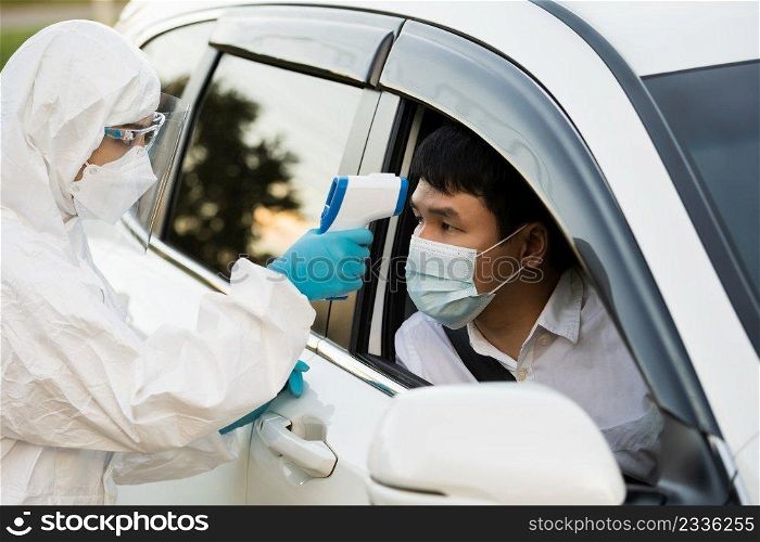 doctor in protective PPE suit using infrared thermometer measuring temperature of man at drive thru station, IR Thermoscan