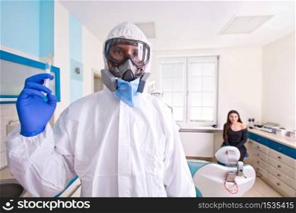 Doctor in protective suit uniform and mask holds injection syringe with vaccine. Female patient waiting for a vaccine. Coronavirus outbreak. Covid-19 concept.