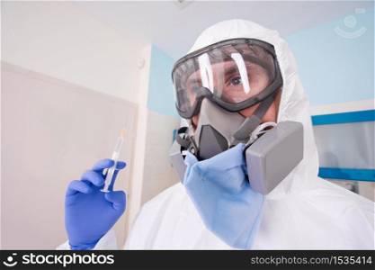 Doctor in protective suit uniform and mask holds injection syringe with vaccine. Coronavirus outbreak. Covid-19 concept.
