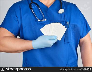 doctor in sterile latex gloves and blue uniform holds a blank white business card, template for the inscription of contacts