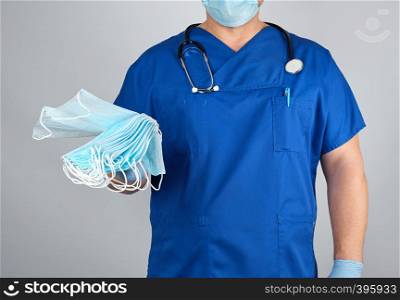 doctor in uniform and in blue latex gloves keeps sterile masks, gray background