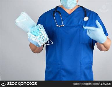 doctor in uniform and in blue latex gloves keeps sterile masks, gray background