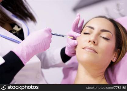 Doctor injecting hyaluronic acid into the cheekbones of a middle-aged woman as a facial rejuvenation treatment.. Doctor injecting hyaluronic acid into the cheekbones of a woman as a facial rejuvenation treatment.