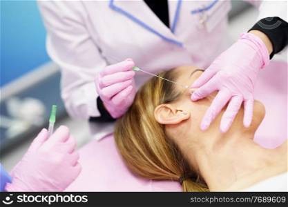 Doctor injecting PDO suture treatment threads into the face of a middle-aged woman.. Doctor injecting PDO suture treatment threads into the face of a woman.