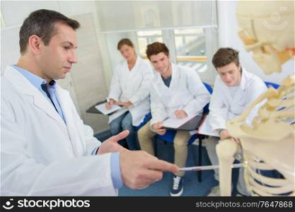 Doctor lecturing students, pointing to skeleton