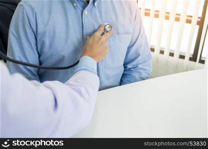 Doctor listening to cheerful young patients chest with stethoscope in his office at the hospital
