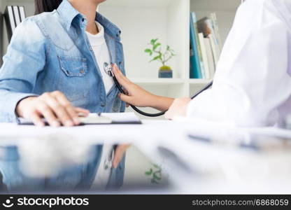 Doctor listening to cheerful young patients chest with stethoscope in his office at the hospital.