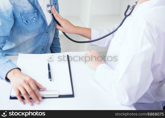 Doctor listening to cheerful young patients chest with stethoscope in his office at the hospital.