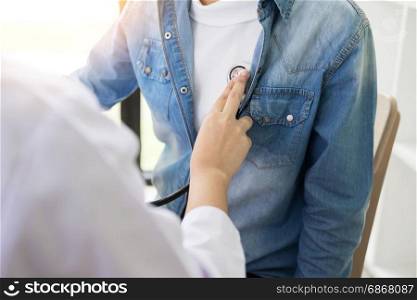 Doctor listening to cheerful young patients chest with stethoscope in his office at the hospital.
