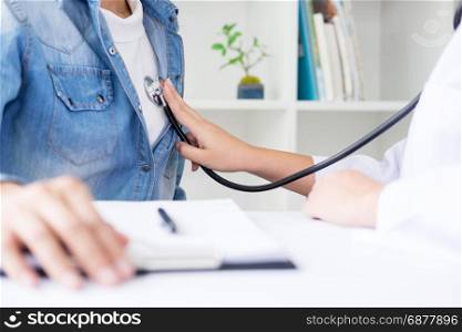 Doctor listening to cheerful young patients chest with stethoscope in his office at the hospital.