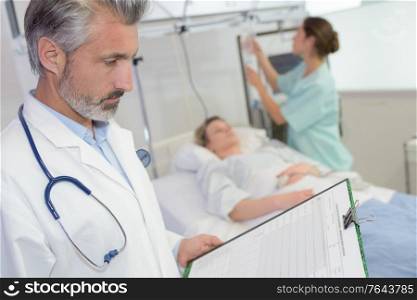Doctor looking at clipboard, patient in background