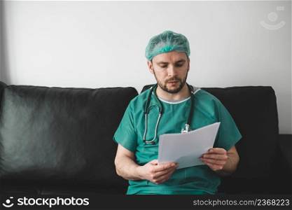 Doctor looking at medical records in the resting room,wearing surgical gown. Doctor looking at medical records in the resting room