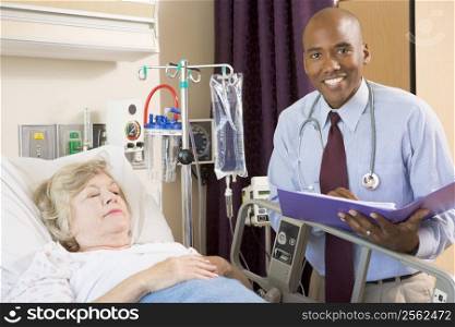 Doctor Making Notes About Senior Woman Lying In Hospital Bed