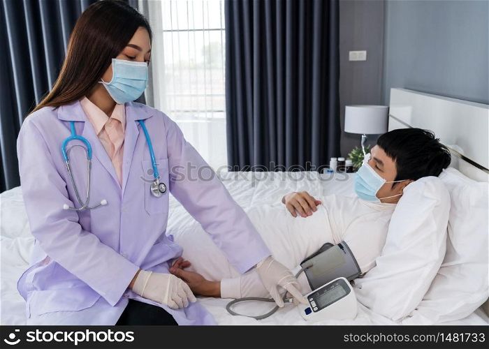 doctor measuring blood pressure of sick man a in bed, people must be wearing medical mask protecting from coronavirus(covid-19) pandemic
