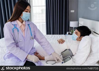 doctor measuring blood pressure of sick man a in bed, people must be wearing medical mask protecting from coronavirus(covid-19) pandemic