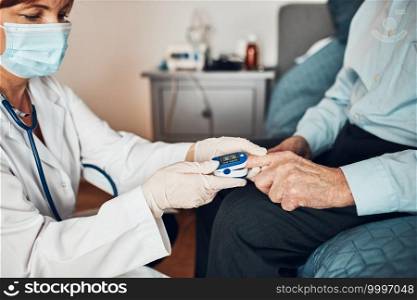 Doctor measuring the degree of oxygen saturation of the blood and heart rate of senior patient using pulse oximeter. Home treatment of virus. Checking health condition. Coronavirus pandemic. Covid-19 outbreak