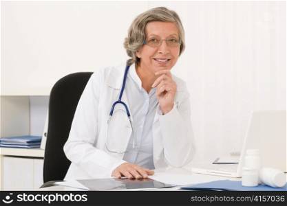Doctor office - senior female physician sit behind desk smiling