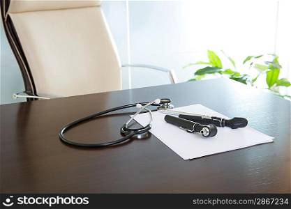 Doctor office table desk and beige chair with stethoscope otoscope and white paper