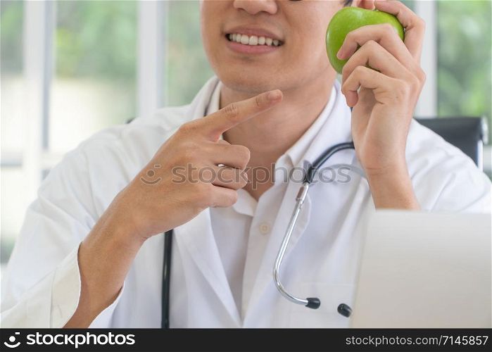 Doctor or nutritionist hold green apple and point your finger at the apple in and smile in clinic. Healthy diet. Concept of nutrition food as a prescription for good health, fruit is medicine