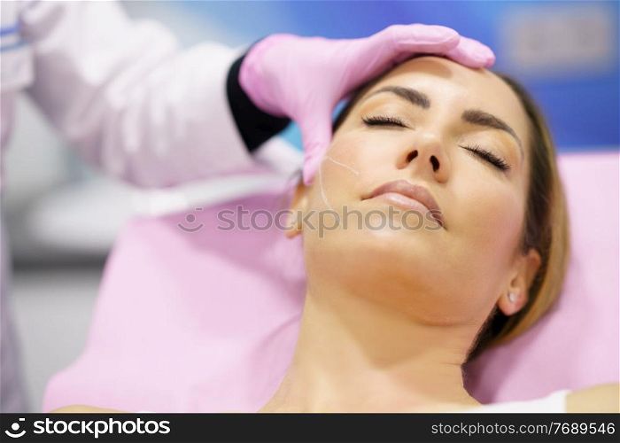Doctor painting the area of a middle-aged woman&rsquo;s face where the PDO suture treatment threads will be injected.. Doctor painting the area of a woman&rsquo;s face where the PDO suture treatment threads will be injected.