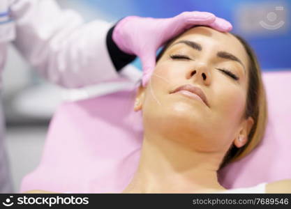 Doctor painting the area of a middle-aged woman&rsquo;s face where the PDO suture treatment threads will be injected.. Doctor painting the area of a woman&rsquo;s face where the PDO suture treatment threads will be injected.