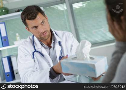 doctor passing box of tissues to patient