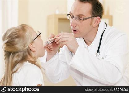 Doctor - Pediatrician - with a child patient in his practice, examining the throat