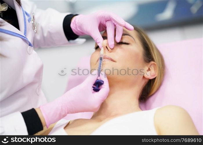 Doctor performing rhinoplasty by injection of hyaluronic acid in the nose of his patient, a middle-aged woman.. Doctor performing rhinoplasty by injection of hyaluronic acid in the nose of his patient.