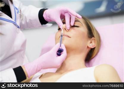 Doctor performing rhinoplasty by injection of hyaluronic acid in the nose of his patient, a middle-aged woman.. Doctor performing rhinoplasty by injection of hyaluronic acid in the nose of his patient.