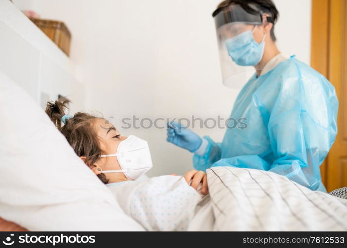 Doctor protected by personal protective equipment examining a little girl with a stethoscope at home.. Doctor examining a little girl with a stethoscope at home.