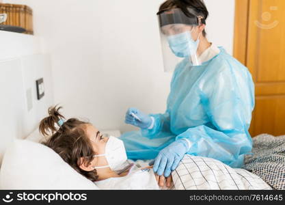 Doctor protected by personal protective equipment examining a little girl with a stethoscope at home.. Doctor examining a little girl with a stethoscope at home.