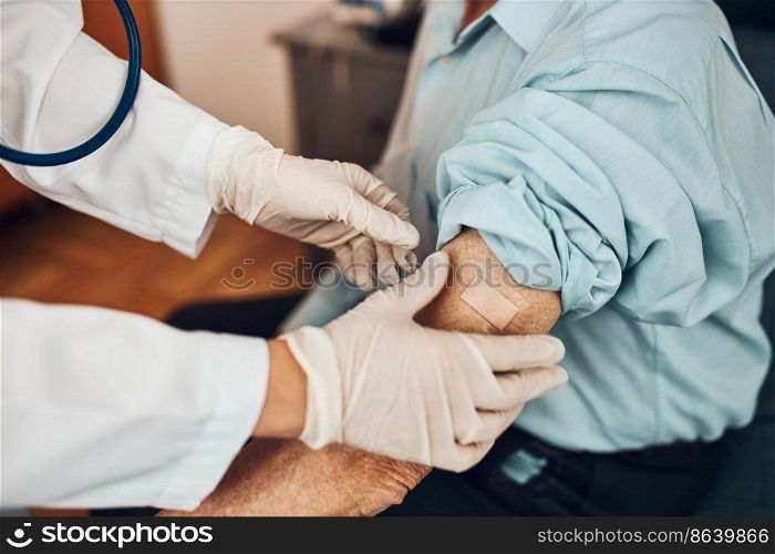 Doctor putting a plaster in place of injection of vaccine to senior man patient. Covid-19 or coronavirus vaccination. Physician wearing white coat and gloves using face mask