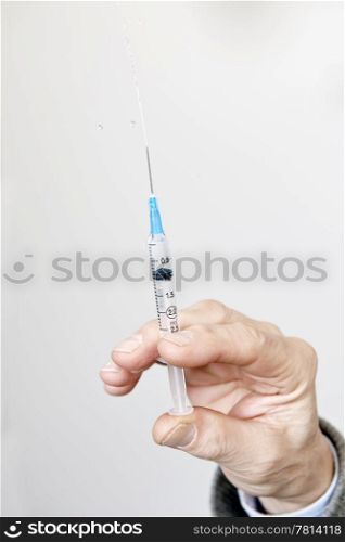 Doctor&rsquo;s hand holding a syringe, and spraying the liquid inside upwards out of the needle