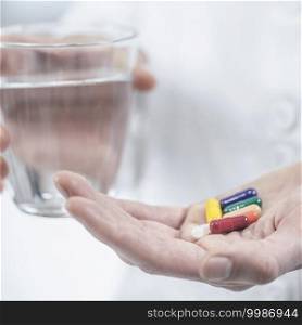 Doctor s hand holding colorful pills and glass of water. Hands with Colorful Pills and a Glass of Water