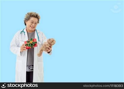 Doctor senior asia woman, medical professional with stethoscope holding teddy bear and a gift box in her hand with smile face.