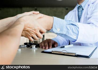 Doctor shakes hands at medical office with patient, wearing glasses, stethoscope and lab coat