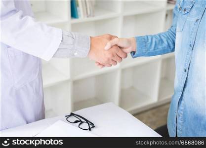 Doctor shakes hands at medical office with patient, wearing glasses, stethoscope and lab coat