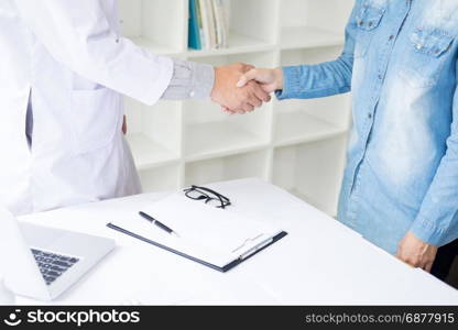 Doctor shakes hands at medical office with patient, wearing glasses, stethoscope and lab coat