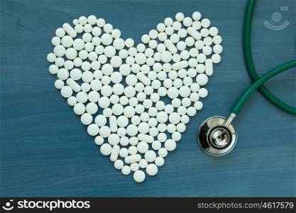 Doctor stethoscope and white pills with heart shape on blue background